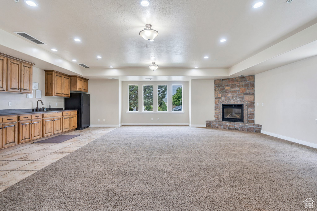 Unfurnished living room featuring light colored carpet, baseboards, recessed lighting, a raised ceiling, and a stone fireplace