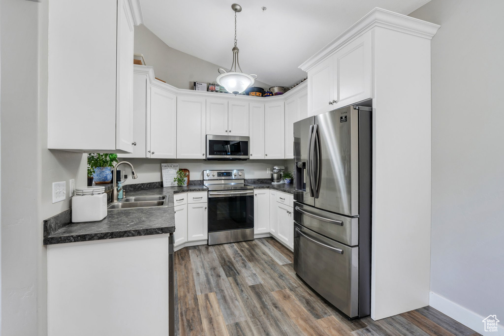 Kitchen featuring appliances with stainless steel finishes, a sink, dark countertops, lofted ceiling, and wood finished floors