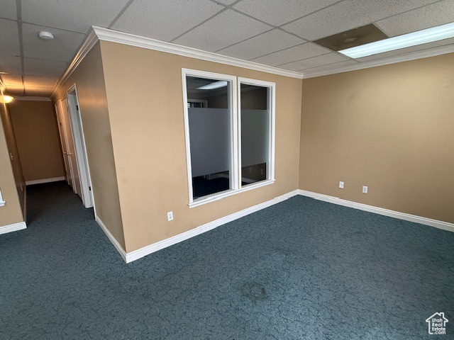 Empty room featuring a drop ceiling, crown molding, dark colored carpet, and baseboards