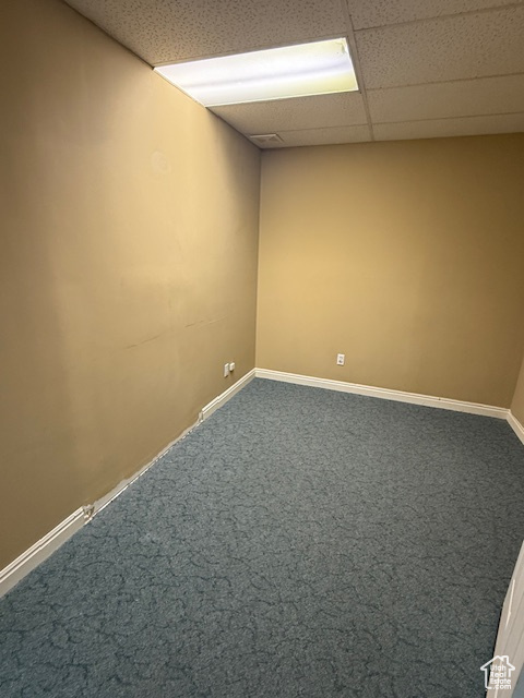 Empty room with dark carpet, a paneled ceiling, and baseboards