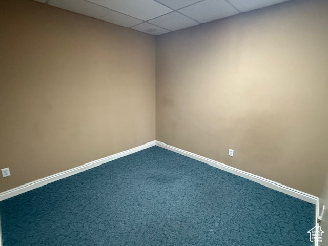 Unfurnished room with baseboards, dark colored carpet, and a paneled ceiling