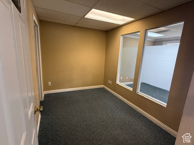 Empty room with carpet flooring, a drop ceiling, and baseboards