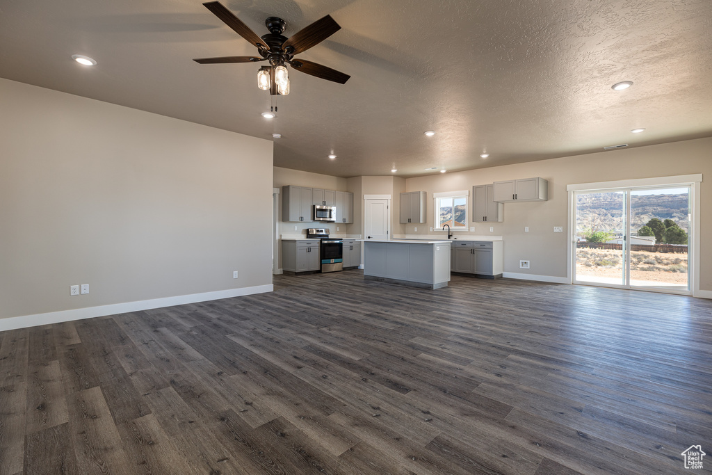 Unfurnished living room with dark wood finished floors, recessed lighting, baseboards, ceiling fan, and a sink