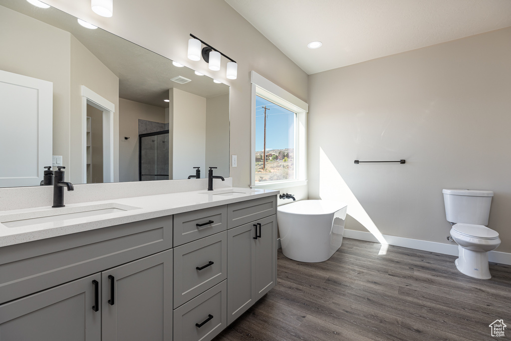 Bathroom featuring a stall shower, wood finished floors, double vanity, a freestanding tub, and toilet