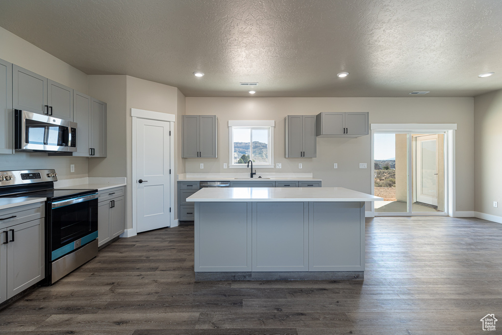 Kitchen featuring appliances with stainless steel finishes, gray cabinets, a center island, dark wood-type flooring, and a textured ceiling