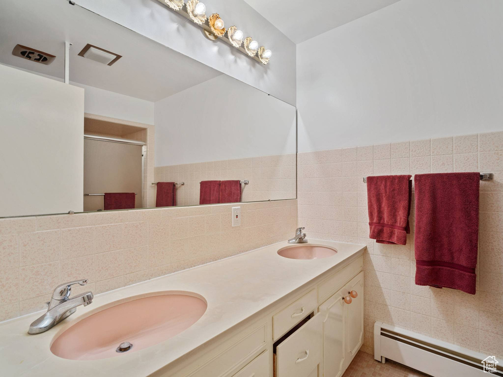 Bathroom featuring a baseboard heating unit, a stall shower, double vanity, and tile walls