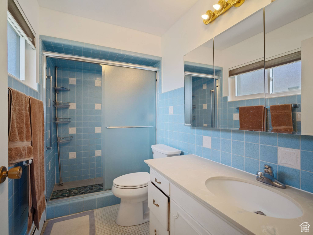 Full bathroom with tile patterned flooring, tile walls, a stall shower, toilet, and vanity