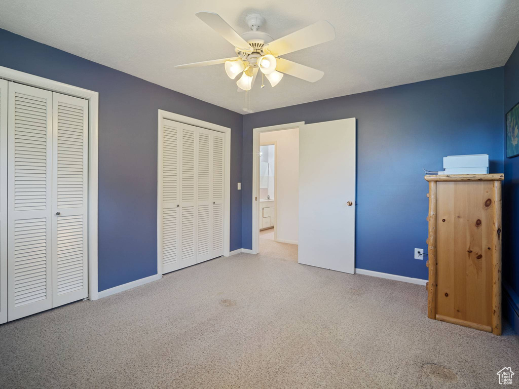 Unfurnished bedroom with two closets, carpet flooring, baseboards, and ceiling fan