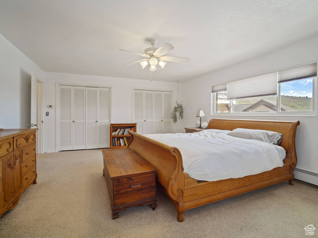 Bedroom featuring multiple closets, light carpet, ceiling fan, and a baseboard heating unit