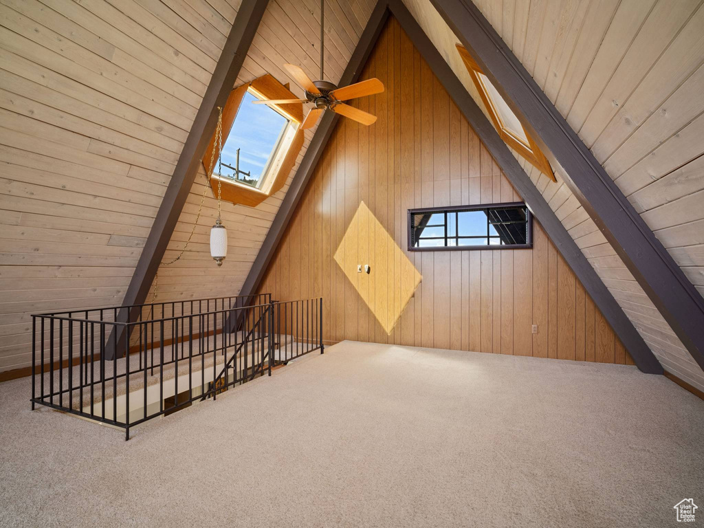 Additional living space with wooden walls, carpet flooring, a skylight, wood ceiling, and ceiling fan