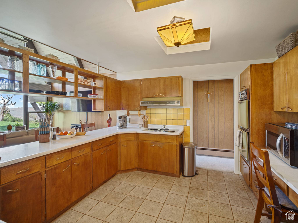 Kitchen featuring stainless steel microwave, under cabinet range hood, light countertops, brown cabinets, and a skylight