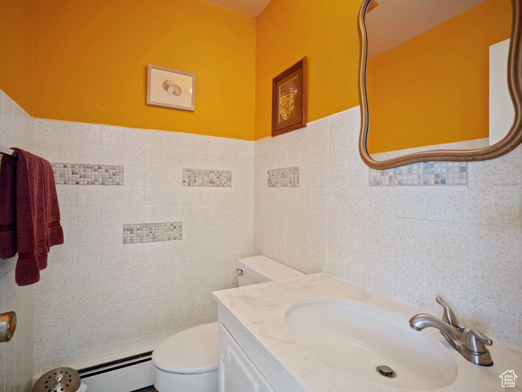 Bathroom with tile walls, a baseboard heating unit, toilet, and vanity