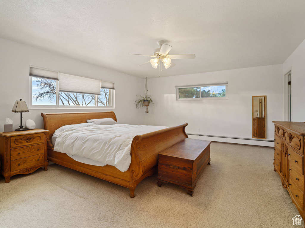 Bedroom with a baseboard radiator, multiple windows, light colored carpet, and a ceiling fan