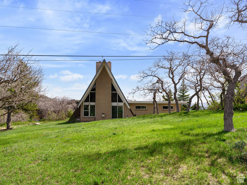 Back of property featuring brick siding, a chimney, and a lawn