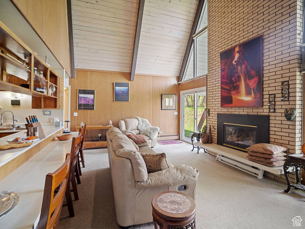 Carpeted living room with beamed ceiling, a fireplace, high vaulted ceiling, wooden walls, and a sink