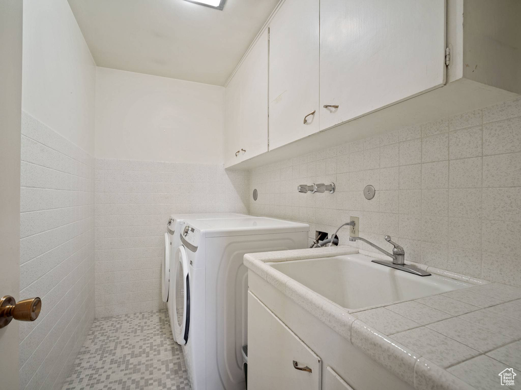 Laundry area with tile walls, washing machine and dryer, and cabinet space