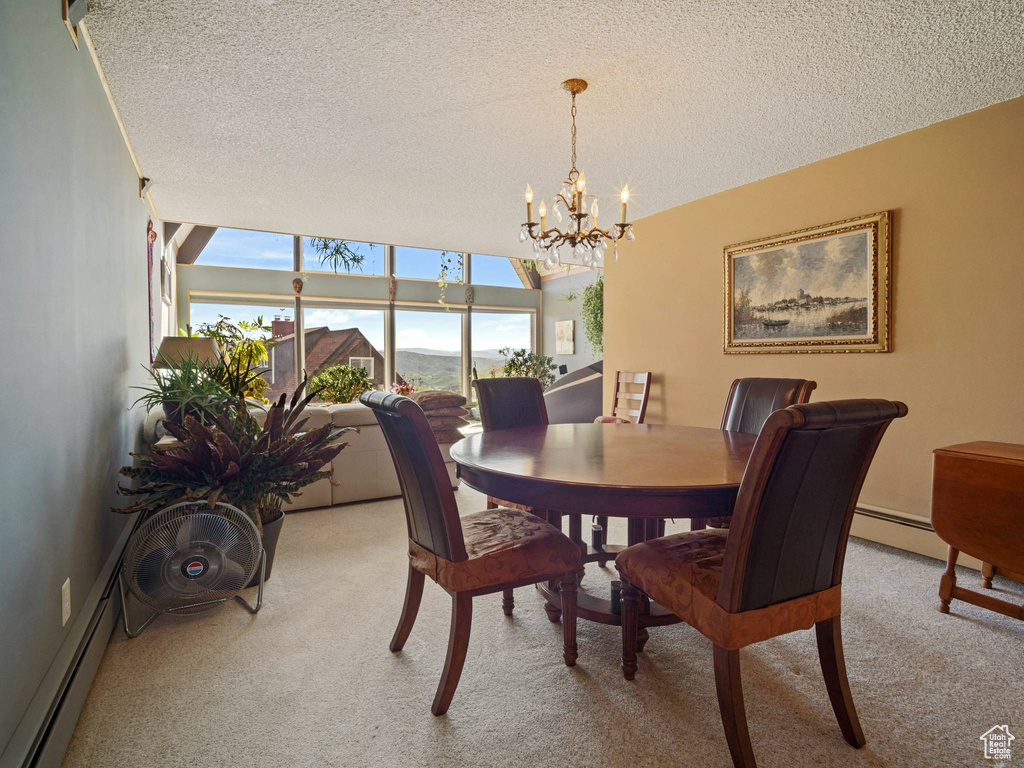 Dining area featuring light colored carpet, a baseboard heating unit, a textured ceiling, and a chandelier