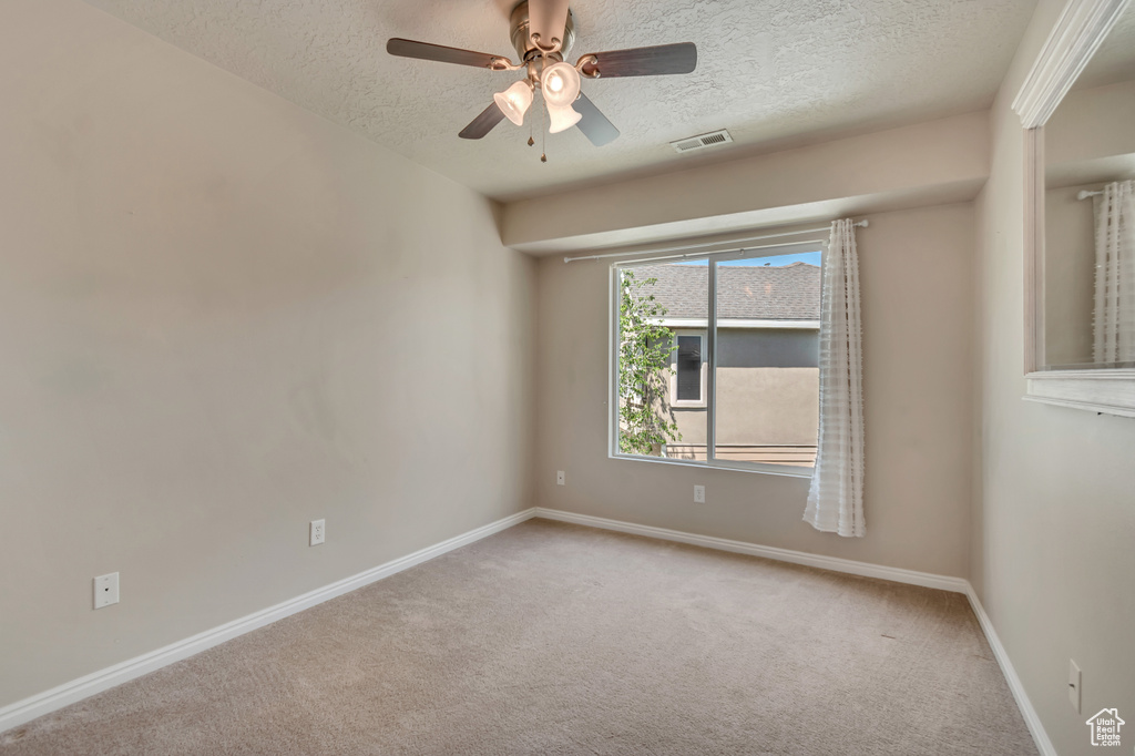 Empty room featuring a textured ceiling, carpet flooring, a ceiling fan, and baseboards