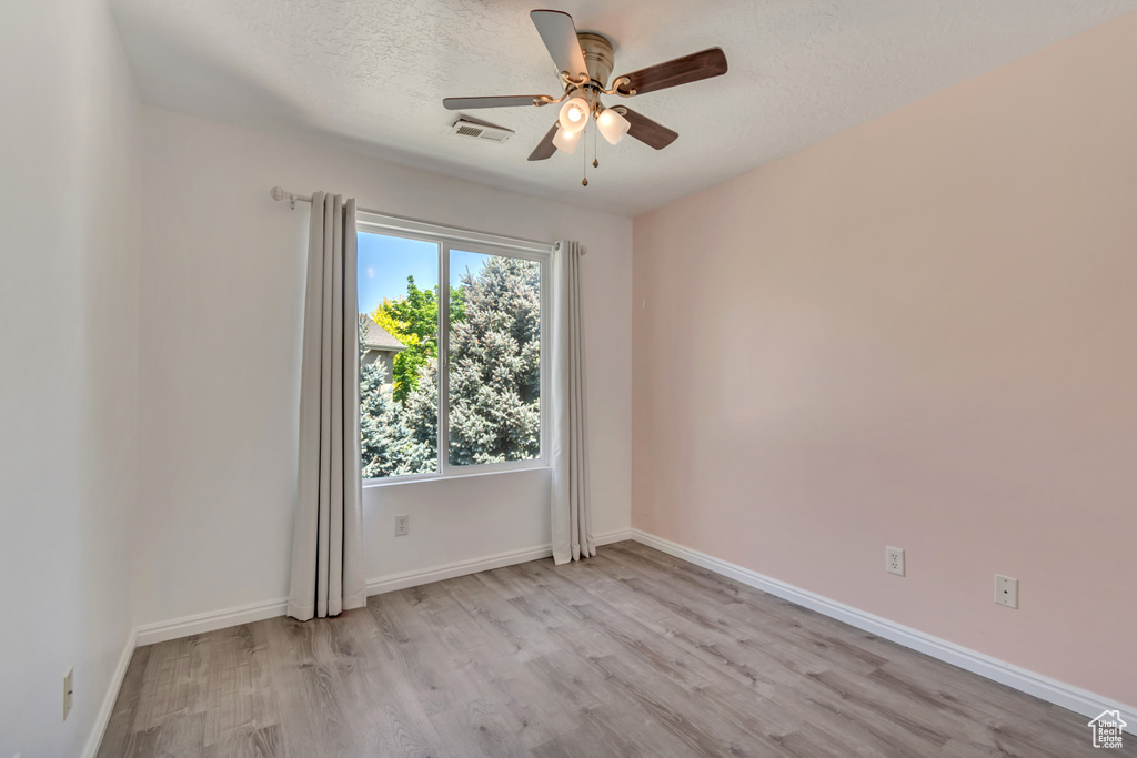 Spare room featuring ceiling fan, light wood finished floors, baseboards, and a textured ceiling