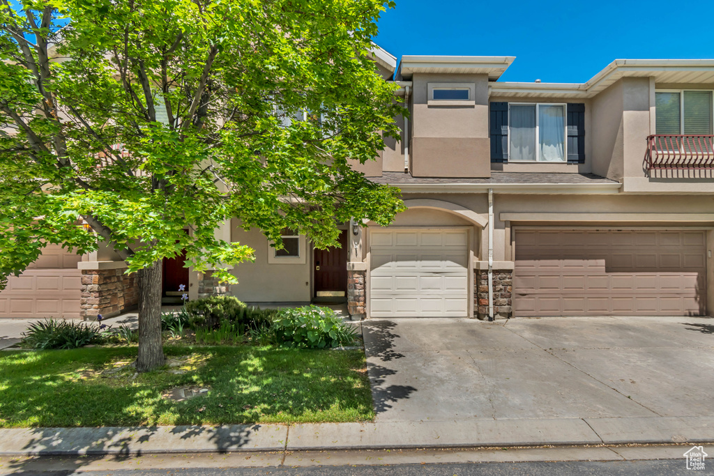 View of front of house with stucco siding, an attached garage, driveway, and stone siding