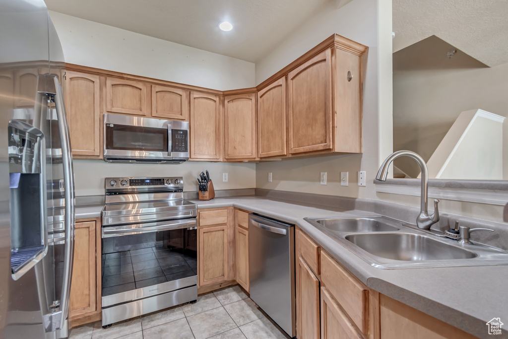 Kitchen with appliances with stainless steel finishes, a sink, light tile patterned flooring, light countertops, and recessed lighting