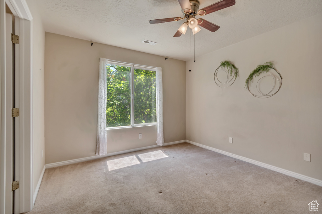 Carpeted spare room featuring baseboards, a ceiling fan, and a textured ceiling