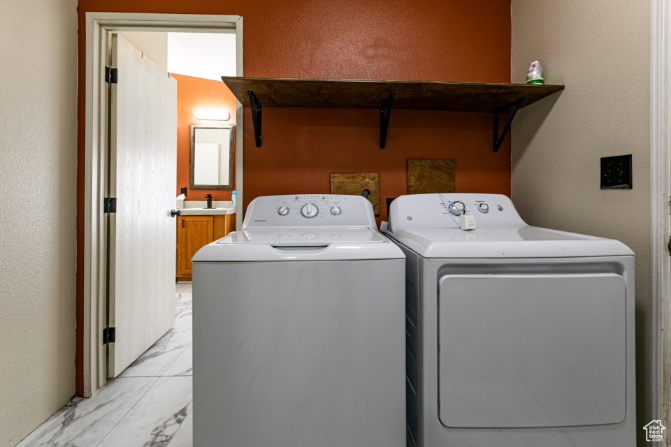 Washroom featuring washer and clothes dryer, light marble finish flooring, a sink, and a textured wall