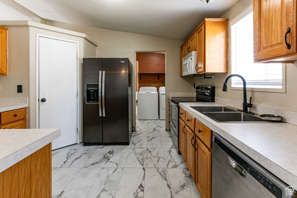Kitchen featuring appliances with stainless steel finishes, washing machine and dryer, a sink, light marble finish flooring, and light countertops