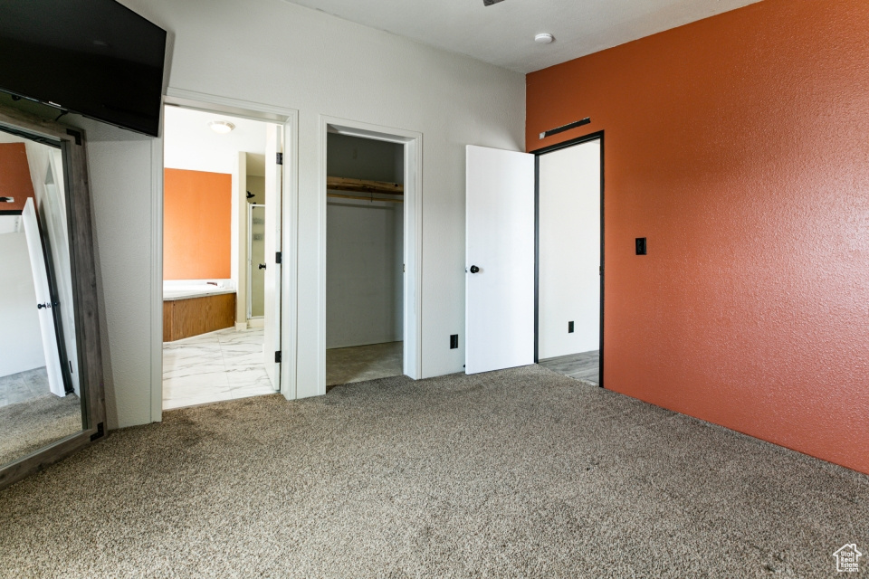 Unfurnished bedroom featuring carpet, a textured wall, ensuite bath, and a closet