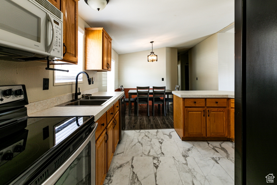 Kitchen with stainless steel range with electric stovetop, white microwave, a sink, brown cabinetry, and light countertops