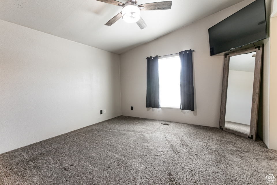 Carpeted empty room with ceiling fan and vaulted ceiling