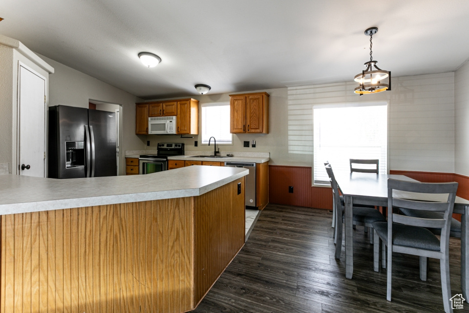 Kitchen featuring appliances with stainless steel finishes, light countertops, dark wood-style flooring, a peninsula, and a sink