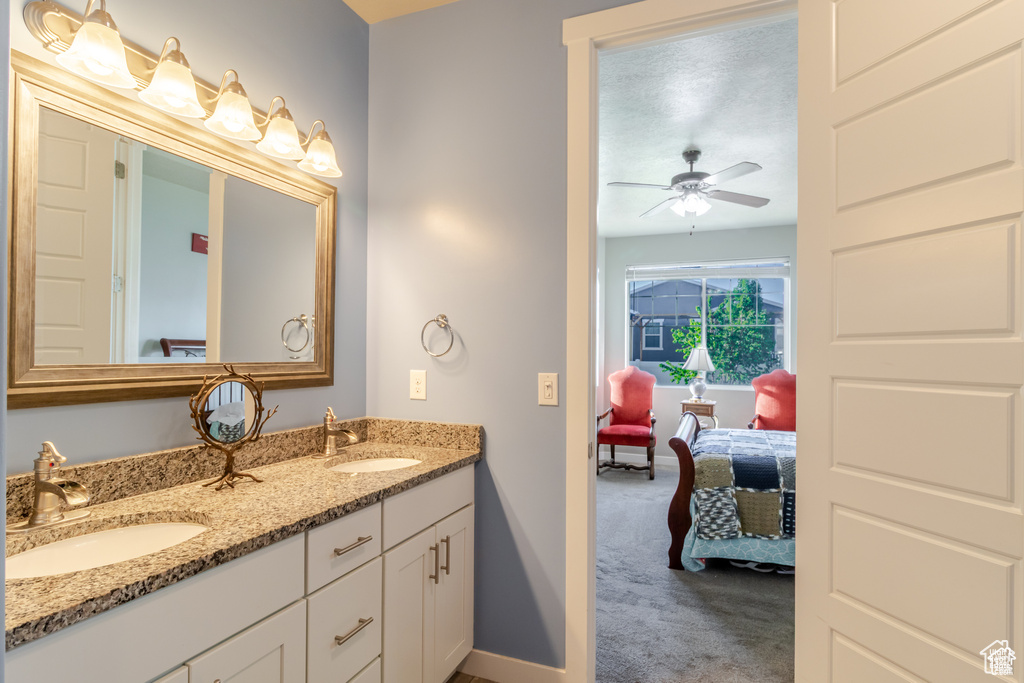 Full bath with ensuite bathroom, double vanity, ceiling fan, and baseboards
