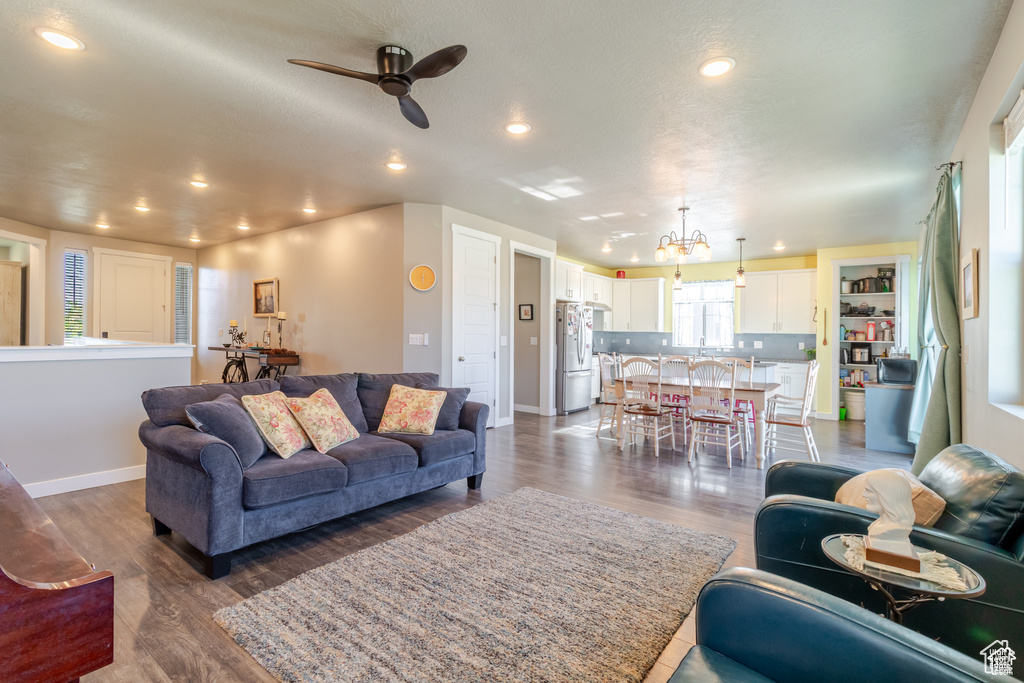 Living room featuring a ceiling fan, recessed lighting, baseboards, dark wood finished floors, and a chandelier