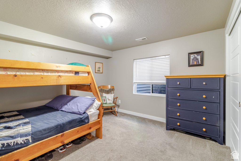 Bedroom featuring light carpet, a textured ceiling, and baseboards