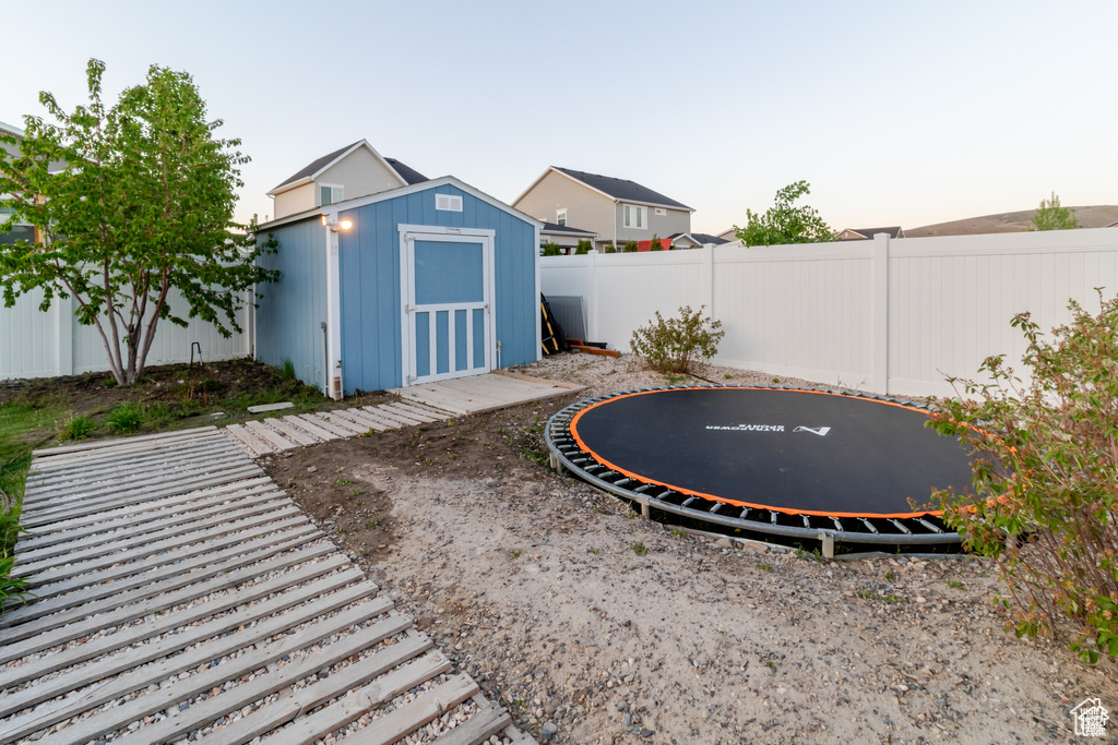 Fenced backyard featuring a trampoline, a shed, and an outdoor structure