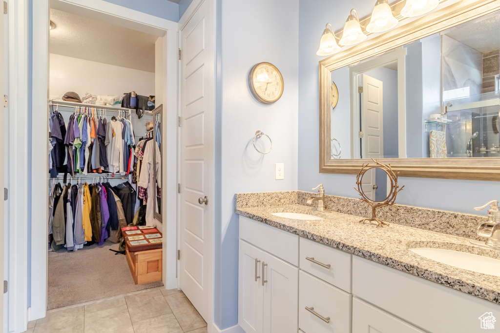Full bathroom featuring a walk in closet, double vanity, and tile patterned flooring