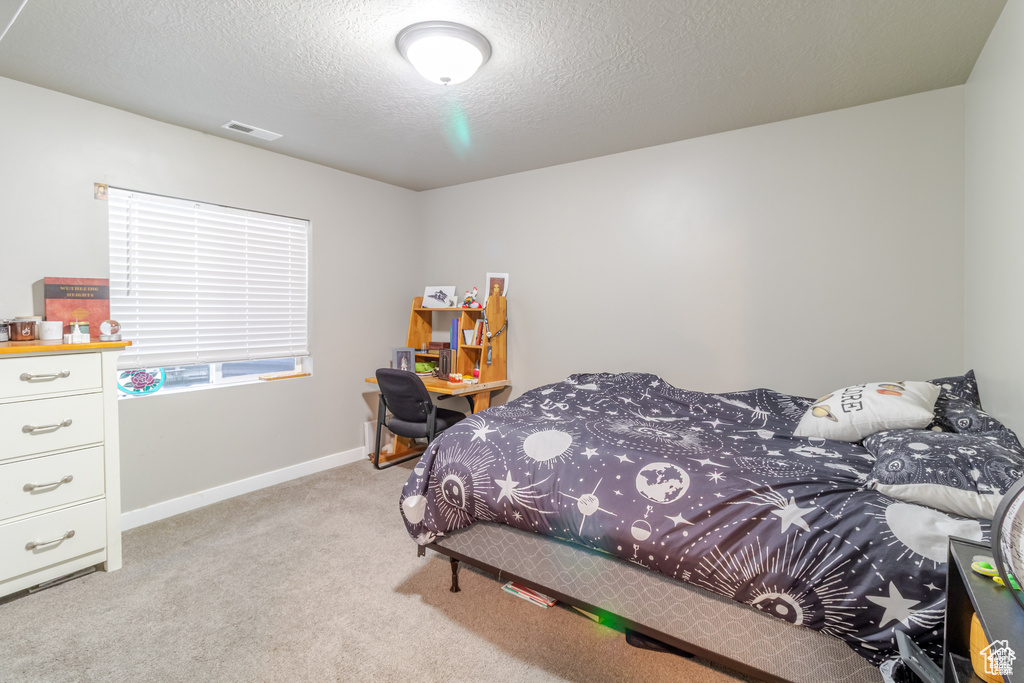 Bedroom featuring light carpet, baseboards, and a textured ceiling
