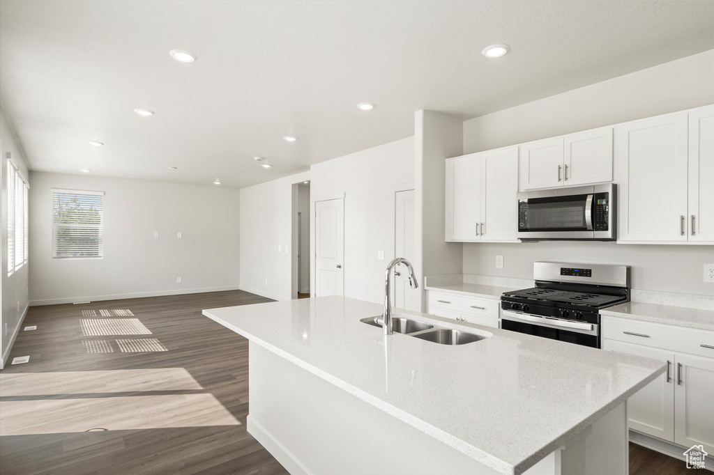 Kitchen featuring stainless steel appliances, dark wood-style flooring, white cabinets, a center island with sink, and recessed lighting