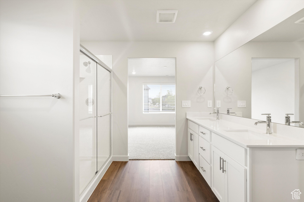 Bathroom with double vanity, a shower stall, wood finished floors, and recessed lighting