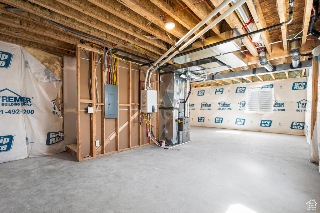 Unfinished basement featuring heating unit, electric panel, and tankless water heater