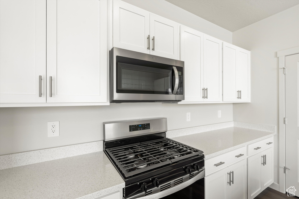Kitchen with stainless steel appliances, white cabinetry, and light stone counters