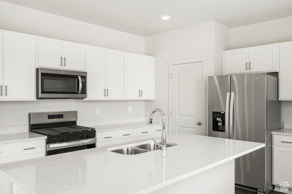 Kitchen with appliances with stainless steel finishes, a kitchen island with sink, white cabinetry, light stone counters, and recessed lighting
