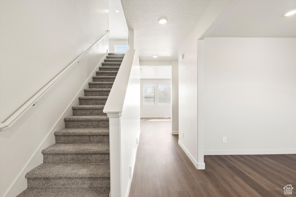 Stairway with wood finished floors, recessed lighting, and a textured ceiling