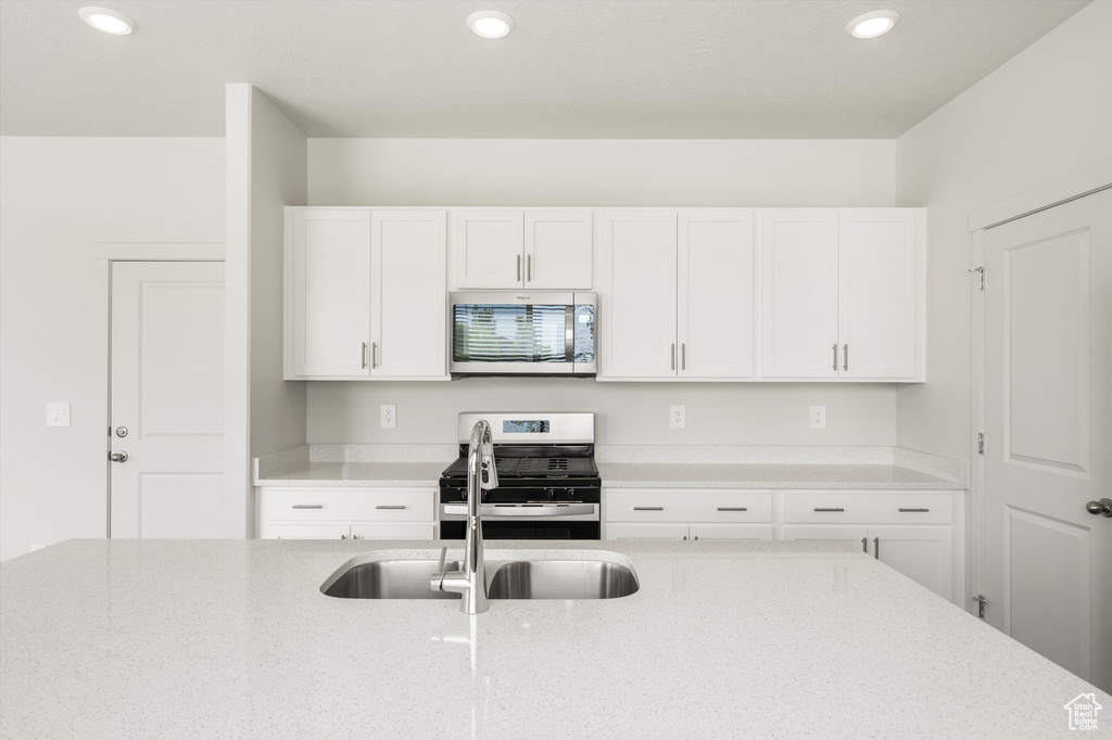 Kitchen with appliances with stainless steel finishes, light stone counters, white cabinetry, and recessed lighting