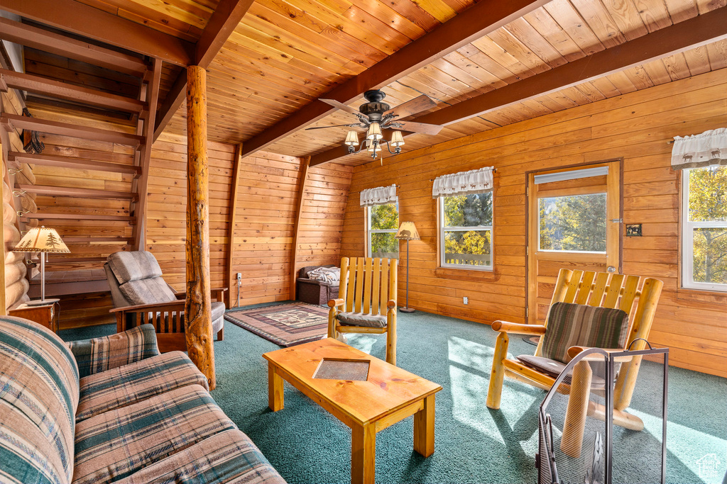 Living area featuring beam ceiling, wooden walls, wooden ceiling, ceiling fan, and carpet