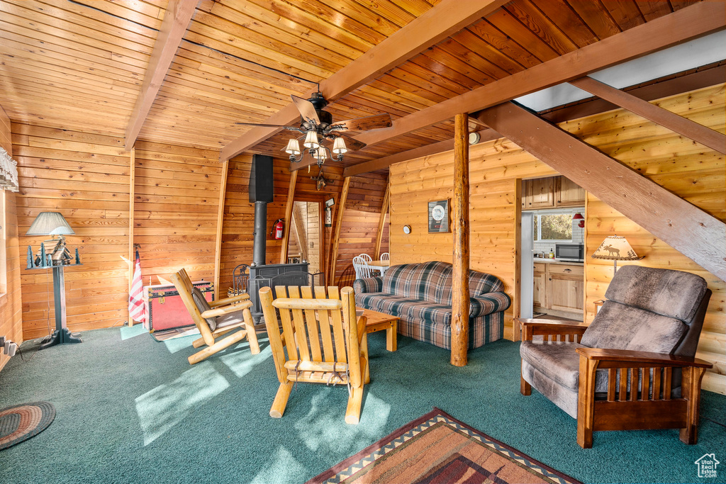 Living area with a wood stove, beamed ceiling, carpet, wooden walls, and a ceiling fan