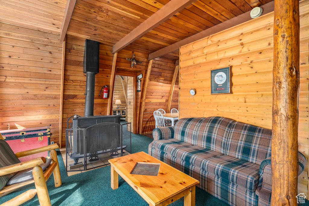 Living area with carpet flooring, wood ceiling, wood walls, a wood stove, and beamed ceiling