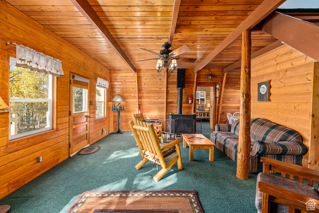Living area with a wood stove, carpet floors, wood walls, wooden ceiling, and a ceiling fan