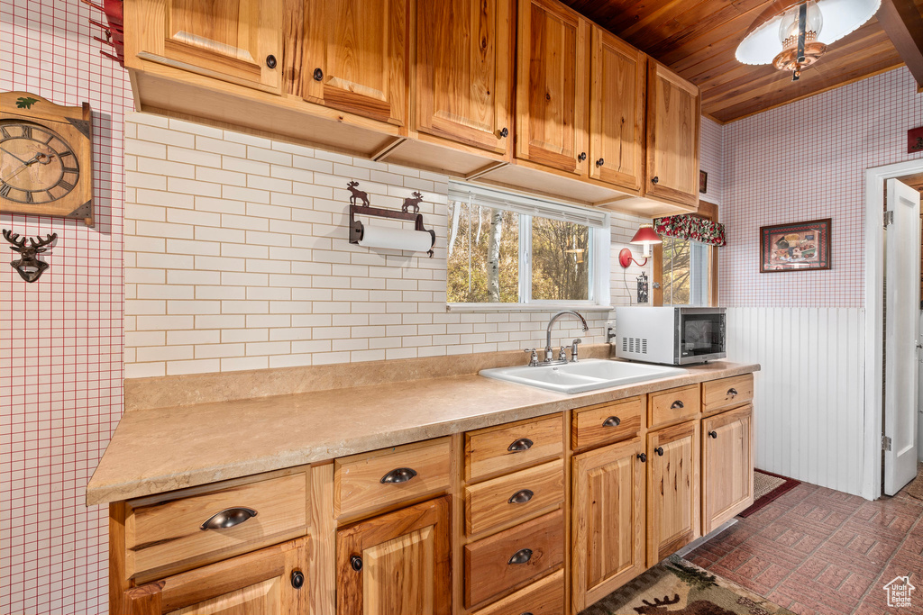 Kitchen featuring stainless steel microwave, wallpapered walls, wooden ceiling, a sink, and light countertops